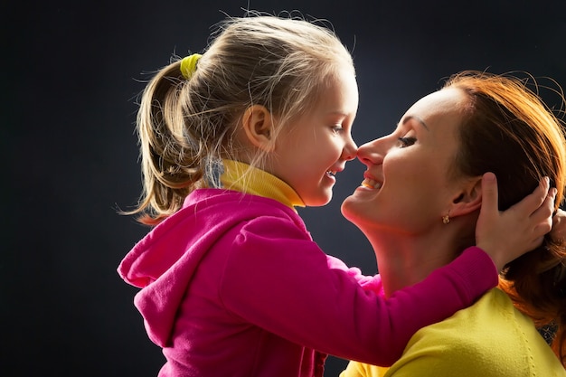 Profile view of little girl hugging her mother smiling over grey background