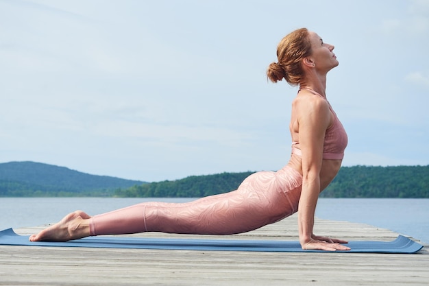 Profile view of a mature woman in pink sportswear practicing yoga