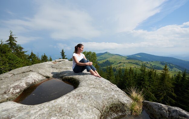 Photo profile view of tourist woman sitting on the top of huge rock