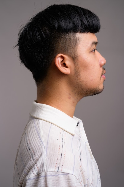 Profile view of young Asian man against gray