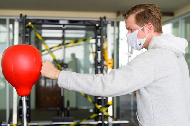 Profile view of young man wearing mask and boxing at the gym