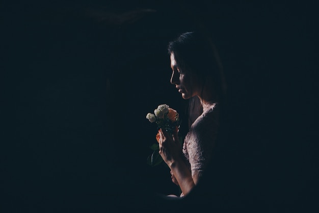 Profile of a woman with flowers. Girl sniffs roses. Silhouette of a lady in the dark