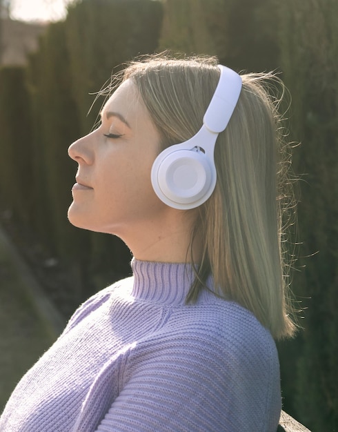 Profile of a woman with white headphones listening to music in the park