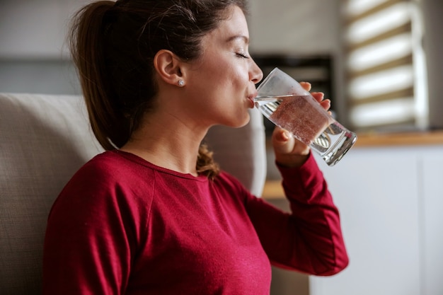 家に座って水を飲む若いブルネットのプロフィール。