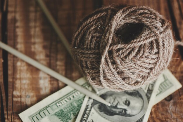 Profitable hobby. earnings on needlework. balls of natural color yarn, knitting needles and money on a wooden table.