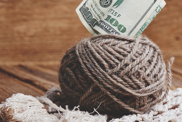 Profitable hobby. Earnings on needlework. Balls of natural color yarn, knitting needles and money on a wooden table.