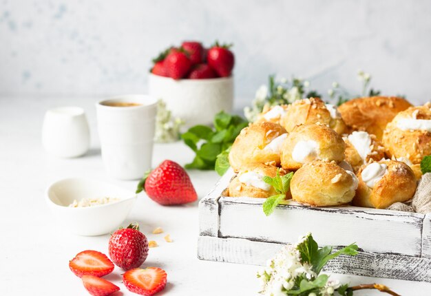 Profiteroles (choux à la crème)-코티지 치즈와 딸기, 민트, 커피 한잔과 함께 크림이 들어간 프랑스 초콜릿 페이스트리 볼.