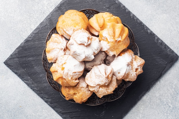 Profiterollen met pudding en poedersuiker op een bord. Betongrijze tafel. Kopieer ruimte.