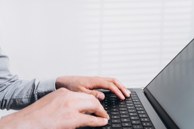 プログラマーの男性がラップトップコンピューターのキーボードで入力し、オフィスのテーブルでインターネットをサーフィンする在宅ビジネスとテクノロジーからの距離学習インターネットネットワーク通信の概念