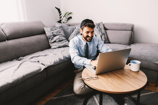 Programmer sitting on the floor in his living room and using laptop during quarantine.