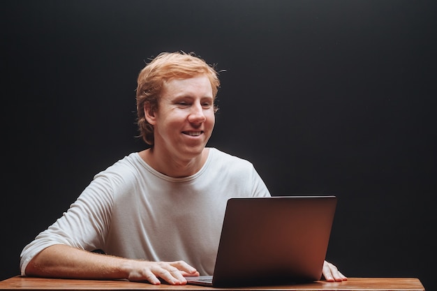 Programmer in a white t shirt on a black background with a laptop