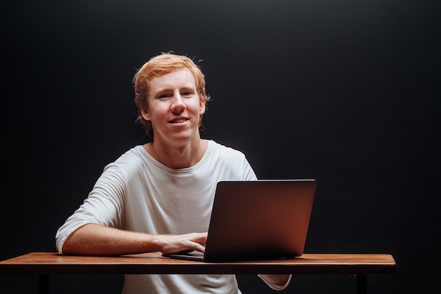 Programmer in a white t shirt on a black background with a laptop