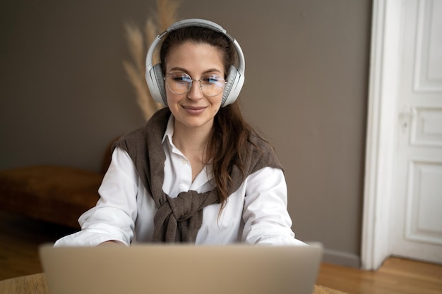 Programmer woman with glasses in the office listening to music\
with headphones break