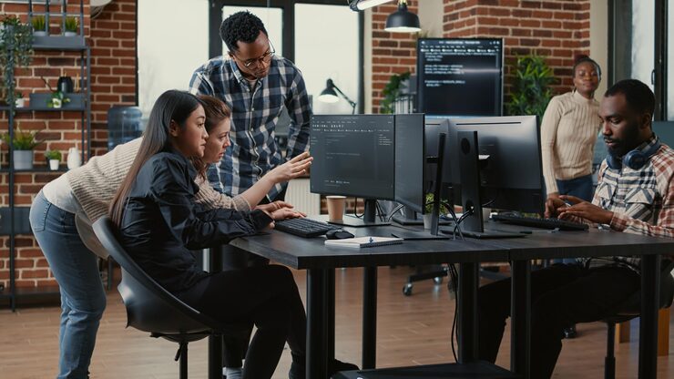 Photo programmers collaborating on group project compiling algorithm for new cloud computing user interface on computer screens. mixed team of software engineers brainstorming ideas looking at running code.