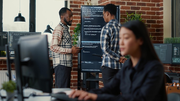 Programmers leaving after analyzing source code on wall screen tv comparing errors using digital tablet with focus switching to programer writing algorithm. Team of coders working on group project.