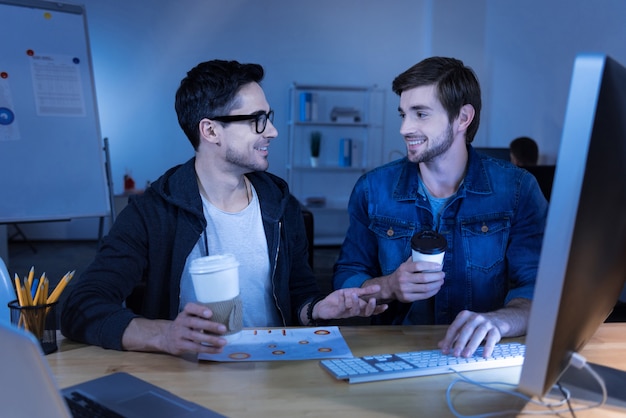 Programmers team. Delighted joyful positive men drinking coffee and interacting with each other while enjoying their work