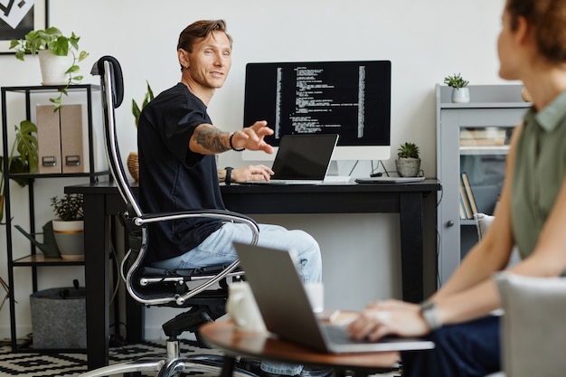 Programmeur bespreekt nieuwe software met zijn collega terwijl ze op de bank zit en op laptop werkt