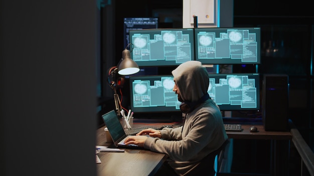 Programming thief breaking through cyber security server and stealing big data on multiple monitors. Hacker with hood using headset and causing computer and system malware with virus. Handheld shot.
