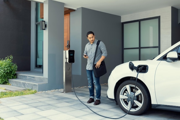 Progressief concept van Aziatische man en elektrische auto met laadstation voor thuis