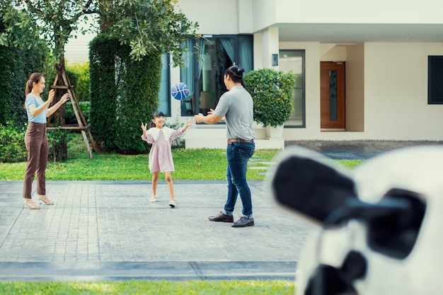 Progressief jong en gelukkig gezin dat in een huis woont met een elektrische auto