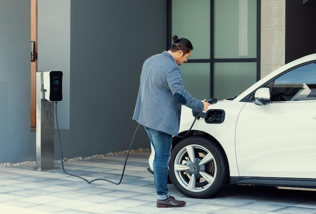 Progressieve aziatische man laadt zijn EV-auto op bij het laadstation thuis