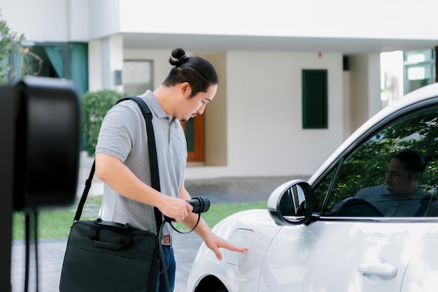 Progressieve aziatische man laadt zijn EV-auto op bij het laadstation thuis