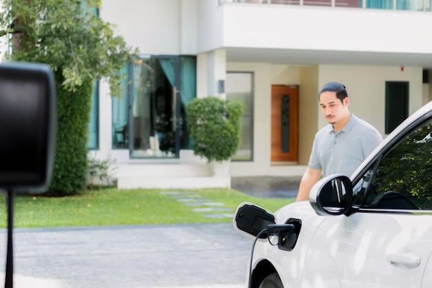 Progressieve aziatische man laadt zijn EV-auto op bij het laadstation thuis
