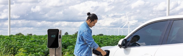 Progressieve man met zijn EV-auto en windturbine als concept van hernieuwbare energie