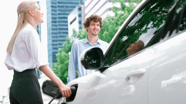 Progressieve zakenman en zakenvrouw installeren laadstekker van laadstation naar elektrische auto voordat ze door het stadscentrum rijden Ecovriendelijke oplaadbare auto aangedreven door schone energie