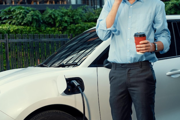 Progressieve zakenman met koffie en EV-auto bij laadstation