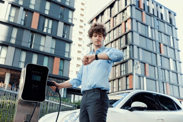 Progressieve zakenman met smartwatch bij openbaar laadstation voor EV-auto