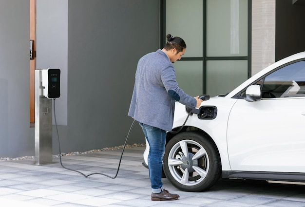 Progressive asian man recharge his EV car at home charging station