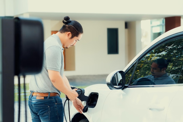 진보적인 아시아 남자가 집 충전소에서 EV 자동차를 충전합니다.