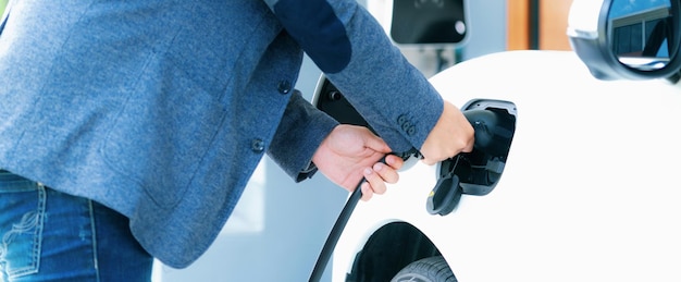 Прогрессивный азиатский мужчина заряжает свой электромобиль на домашней зарядной станции
