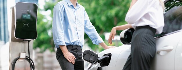 Progressive businessman and businesswoman at charging point and EV car