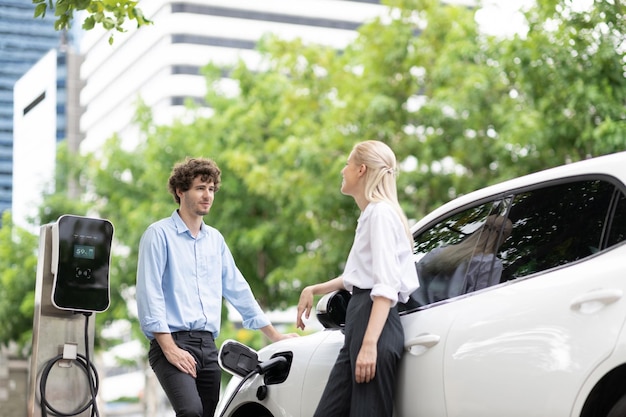 充電ポイントと EV 車で進歩的なビジネスマンとビジネスウーマン