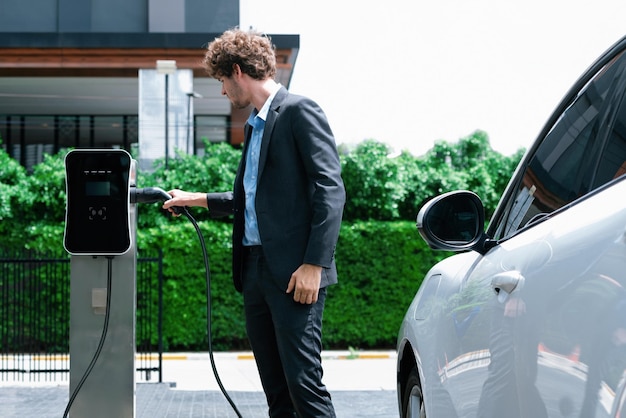 Progressive businessman charging EV car at public parking car charging station