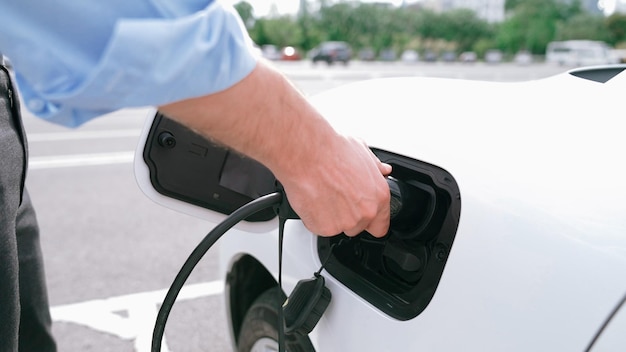 Progressive businessman install charger plug from charging station to his electric car before driving around city center Eco friendly rechargeable car powered by sustainable and clean energy