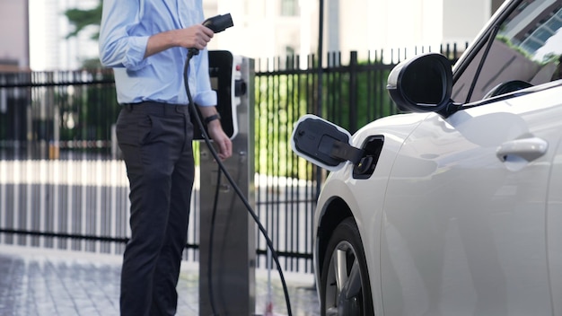 Progressive businessman install charger plug from charging station to his electric car before driving around city center Eco friendly rechargeable car powered by sustainable and clean energy