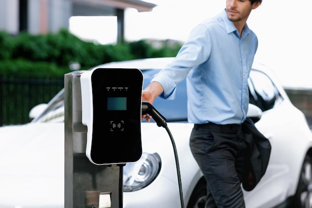 Progressive businessman plugs charger plug from charging station to EV