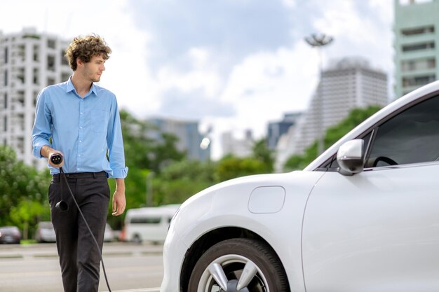 Progressive businessman plugs charger plug from charging station to ev