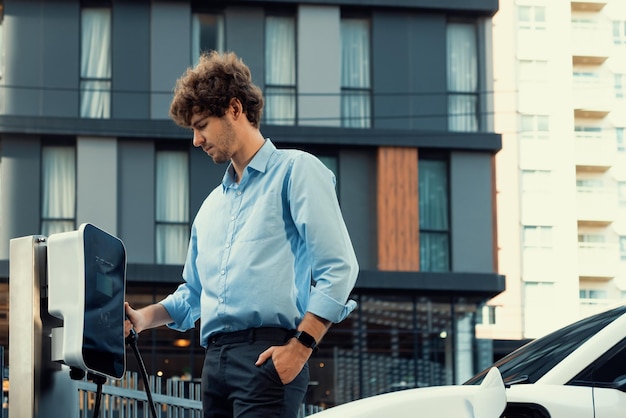 Progressive businessman plugs charger plug from charging station to EV