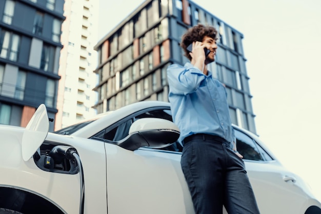 Progressive businessman talking on the phone with recharging electric vehicle