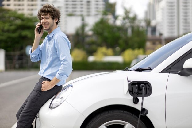 Progressive businessman talking on the phone with recharging electric vehicle