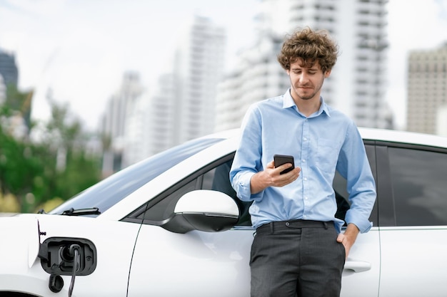 Progressive businessman talking on the phone with recharging electric vehicle