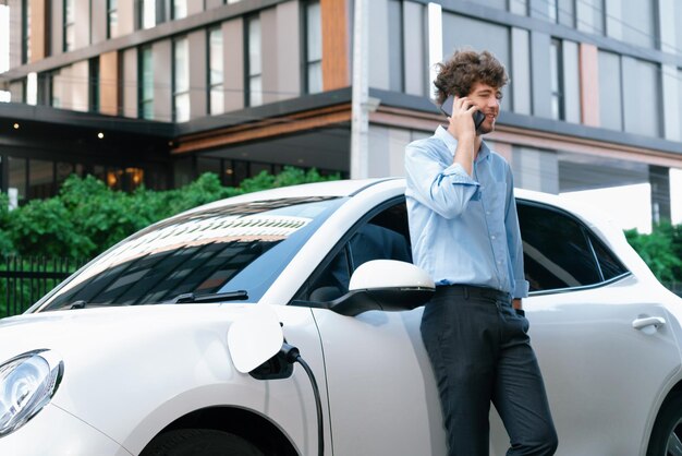 Progressive businessman talking on the phone with recharging electric vehicle