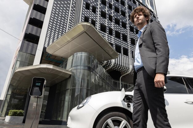 Foto uomo d'affari progressista con auto ev presso la stazione di ricarica per auto parcheggio pubblico