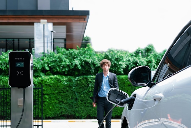 Progressive businessman with EV car at public parking car charging station