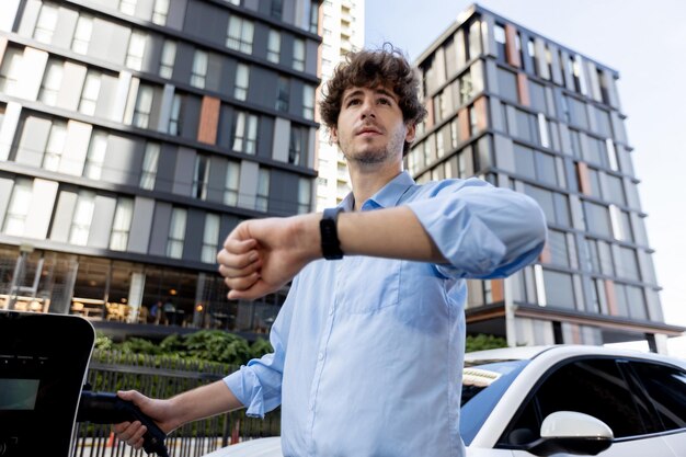 Progressive businessman with smartwatch at public charging station for EV car