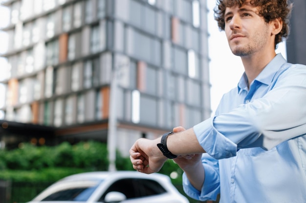 Progressive businessman with smartwatch at public charging station for EV car